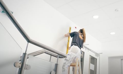 Handwerkerin misst Wandhöhe mit Wasserwaage, konzentriert bei der Montage