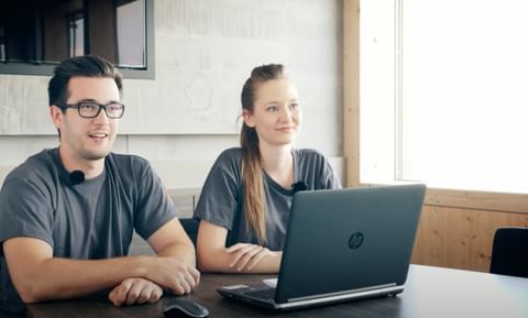 Zwei junge Menschen im Gespräch, lächelnd vor Laptop – locker, sympathisch, echt