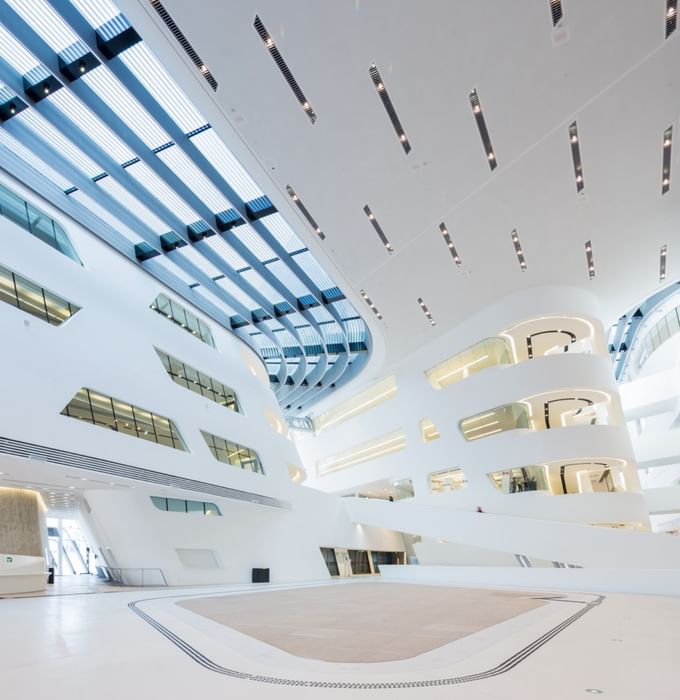 Weitläufiges, lichtdurchflutetes Atrium der Wirtschaftsuniversität Wien mit weißen Wänden, großen Fensterflächen und moderner Architektur.