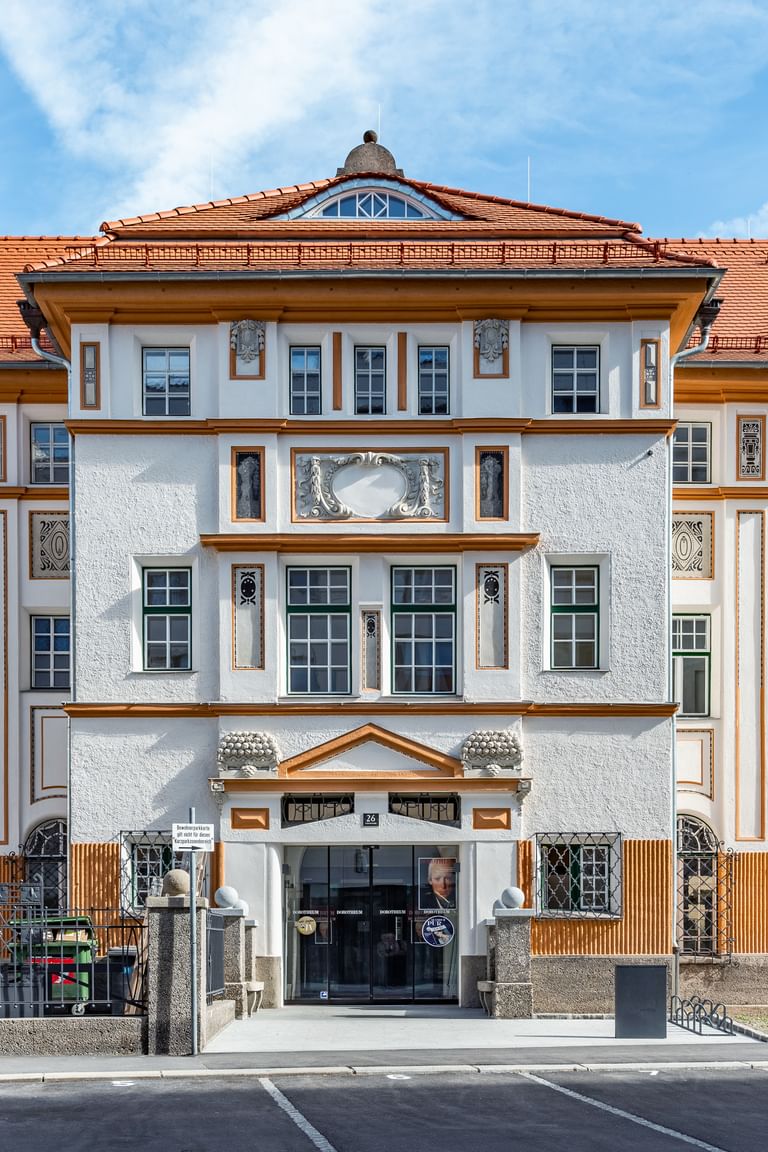Detailreiche Jugendstilfassade des Dorotheum Linz mit aufwendig verzierten Fenstern, geometrischen Ornamenten und markanten orangefarbenen Zierelementen, restauriert mit Histolith-Farben