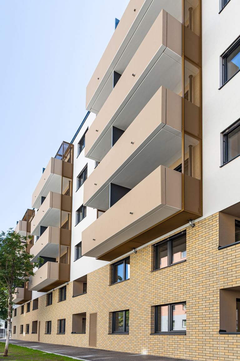 Nahaufnahme Fassade in beiger Klinkeroptik, mit Balkonen, davor Wiese