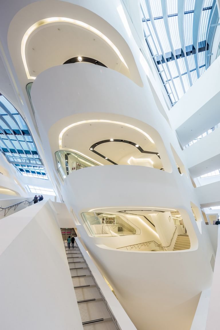 Detailaufnahme eines modernen Treppenaufgangs im Atrium der Wirtschaftsuniversität Wien mit weißen Wänden, runden Formen und viel Tageslicht.