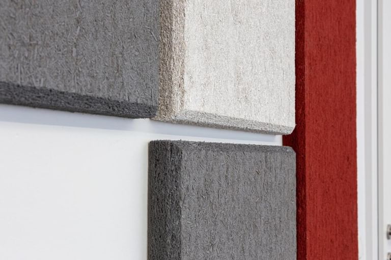 Nahaufnahme strukturierter Hanfpaneele in Grau und Beige an weißer Wand mit rotem Akzent