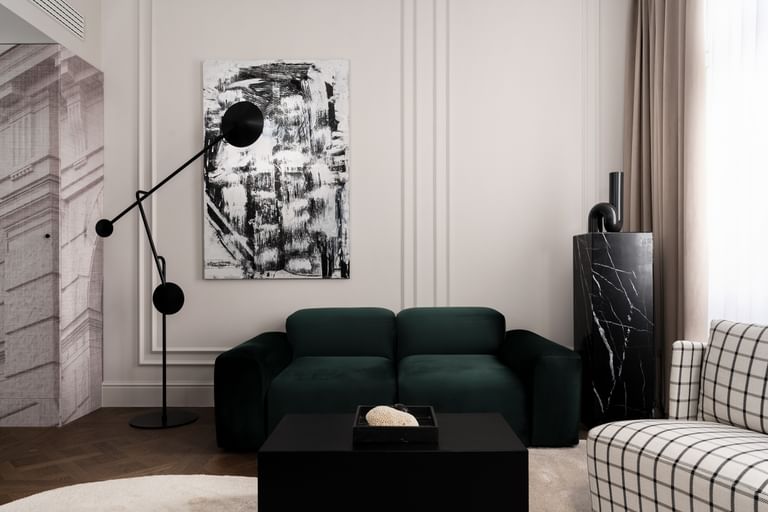 Eleganter Loungebereich einer Executive Suite im „The Amauris“ Wien mit tiefgrünem Samtsofa, großem abstraktem Schwarz-Weiß-Gemälde, skulpturaler schwarzer Stehleuchte, schwarzem Marmorsockel und bodenlangen beigefarbenen Vorhängen.