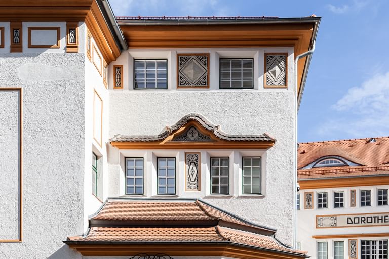 Detailreiche Jugendstilfassade des Dorotheum Linz mit aufwendig verzierten Fenstern, geometrischen Ornamenten und markanten orangefarbenen Zierelementen, restauriert mit Histolith-Farben