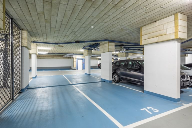 Tiefgarage mit weißen Säulen, blauen Parkflächen und Autos