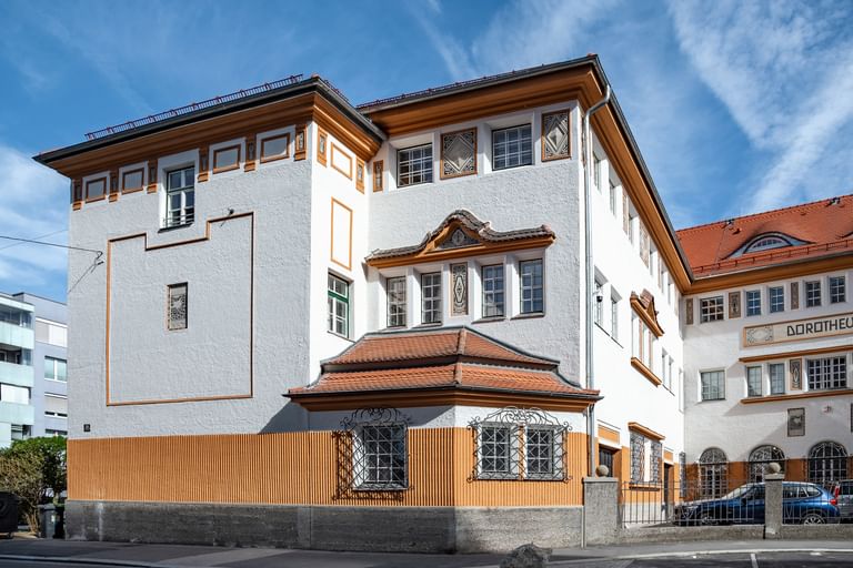 Detailreiche Jugendstilfassade des Dorotheum Linz mit aufwendig verzierten Fenstern, geometrischen Ornamenten und markanten orangefarbenen Zierelementen, restauriert mit Histolith-Farben