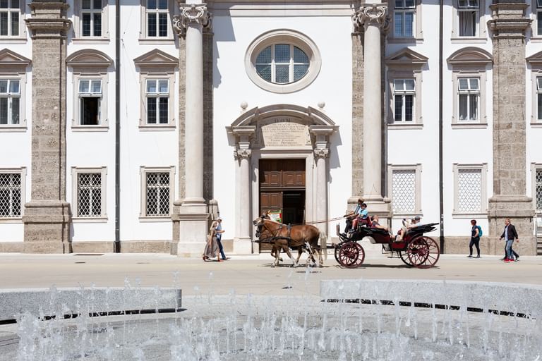 Fontäne-Brunnen, vorbeilaufende Menschen und vorbeifahrender Pferdekutsche vor der Kirche