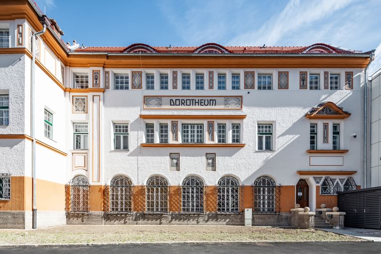 Detailreiche Jugendstilfassade des Dorotheum Linz mit aufwendig verzierten Fenstern, geometrischen Ornamenten und markanten orangefarbenen Zierelementen, restauriert mit Histolith-Farben