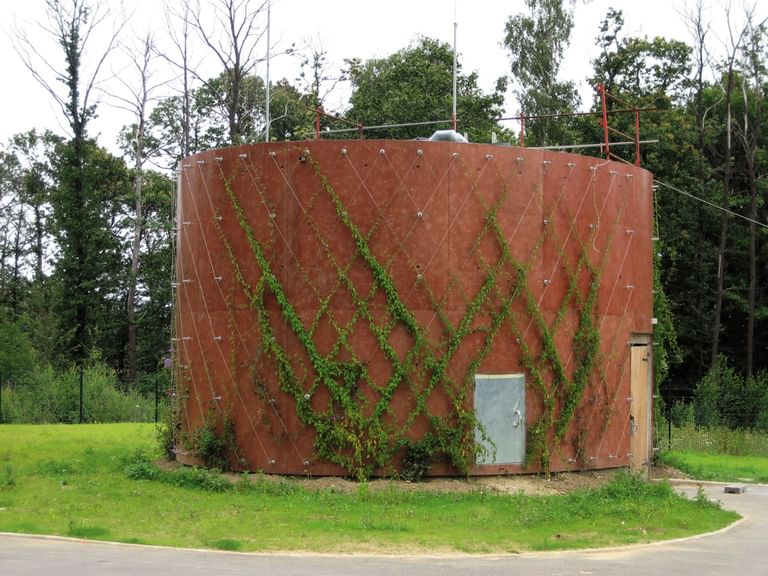 Runder, orange-brauner Wassertank, der von grünen Pflanzen umwachsen ist.