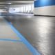 Grauer Boden einer Tiefgarage mit blauen Fahrbahn- und Parkmarkierungen